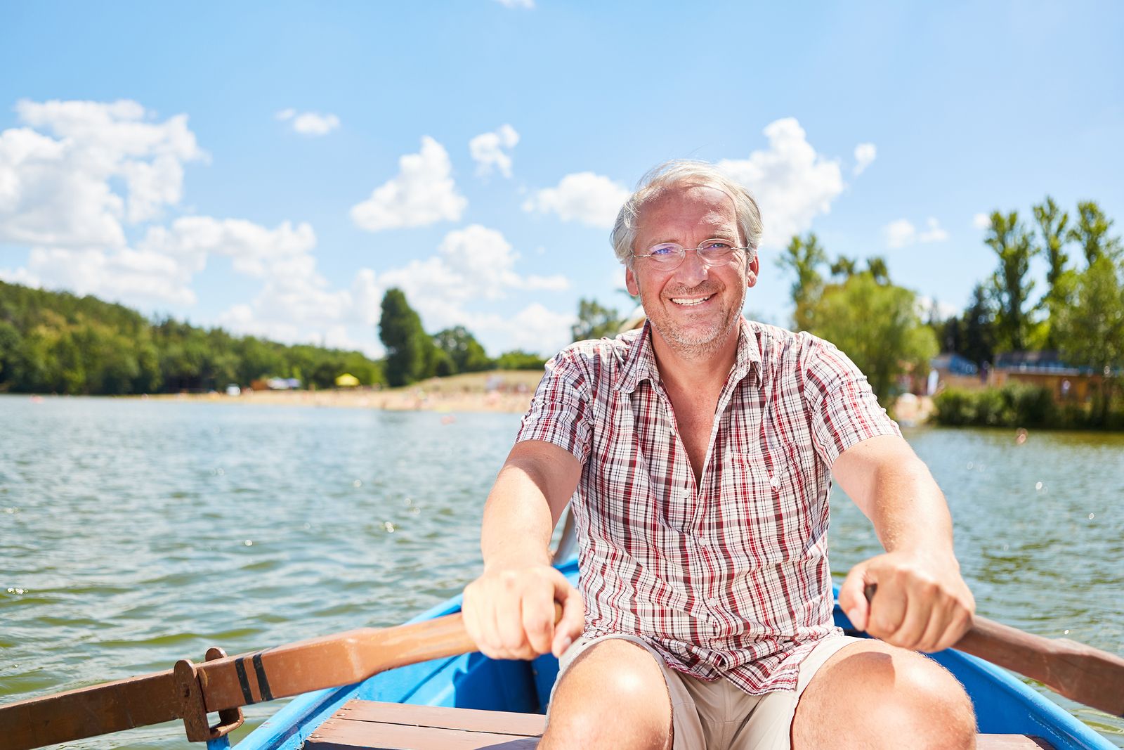 Vital senior man in rowboat on a lake in summer on a weekend
